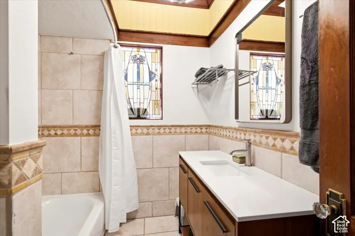 Bathroom featuring a built-in bathtub with shower, vanity with an integrated sink, and an accent stained-glass window