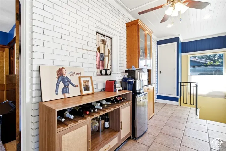 White-painted brick accent wall complemented by wood-finish built-in cabinetry, tile flooring, and a ceiling fan with integrated lighting
