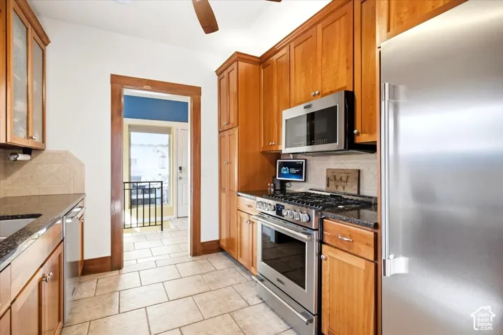 Kitchen featuring wood cabinetry, stainless steel appliances, stone countertops, and tile flooring