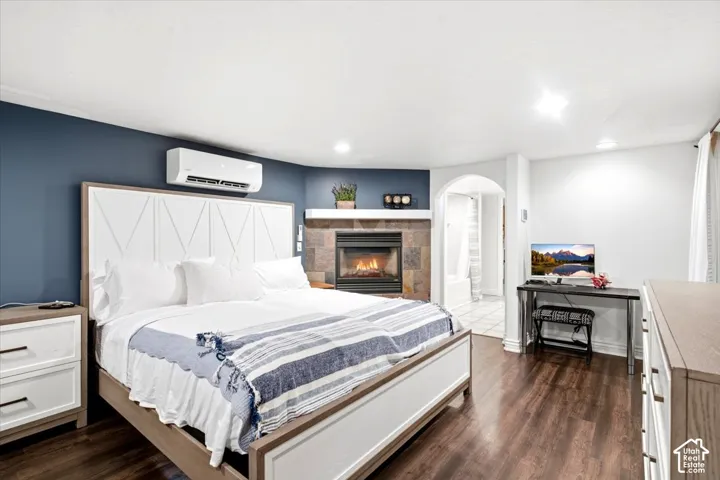 Dark wood-finish flooring, built-in fireplace with stone surround, wall-mounted mini-split system, arched doorway, and recessed ceiling lighting