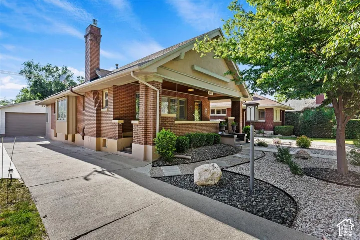 Brick exterior with a covered porch, an attached garage, a bay window, a concrete driveway, and a landscaped rock garden