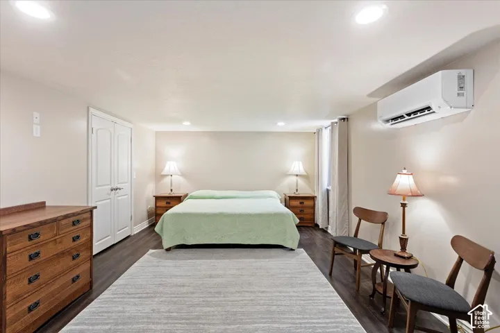 Wood-finish flooring, recessed lighting, double-door closet, window with drapes, and a wall-mounted climate control unit