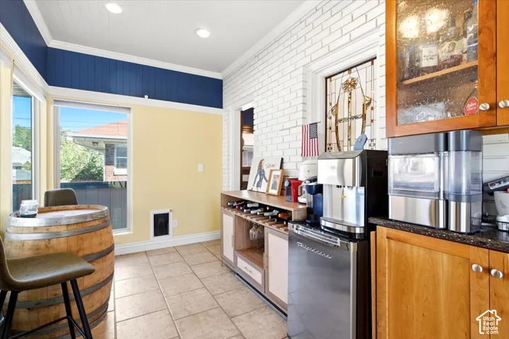 Tiled flooring, built-in wine rack, base cabinets with wood-finish doors, glass-front upper cabinetry, and a refrigerator
