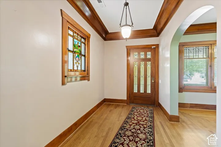 Hardwood flooring, stained glass window detail, wood door with decorative glass inserts, arched entryway, and a hanging pendant light fixture