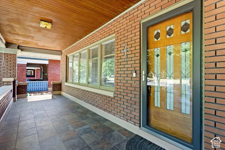 Expansive covered porch featuring brick exterior, wood-paneled ceiling, tiled flooring, and multiple windows with blinds