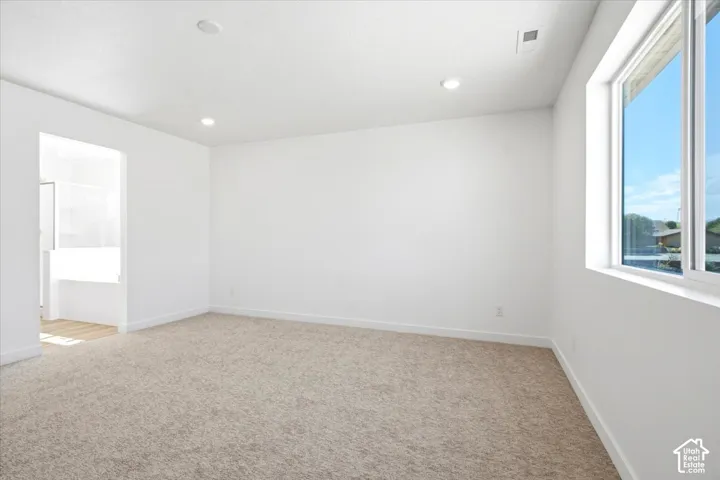 Recessed lighting, light-toned carpet flooring, white walls, and a large window