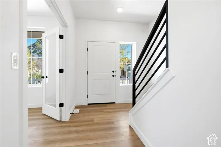 Light wood-finish flooring, white walls, and a black horizontal bar staircase railing