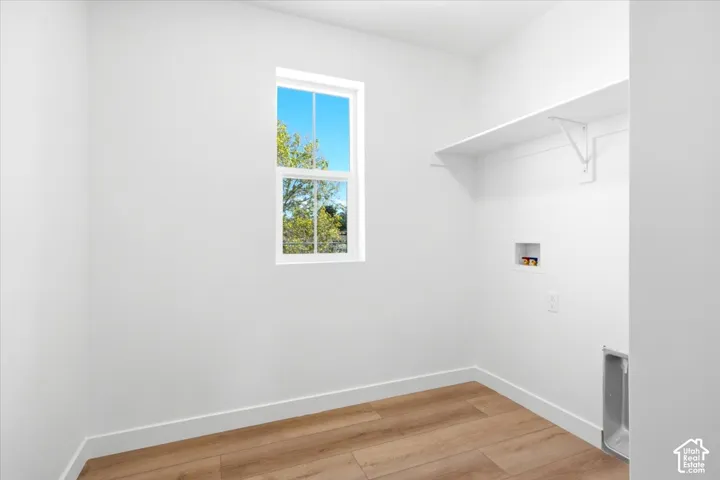 Wood-finish flooring with white baseboards, a white-framed window, and a built-in white shelf