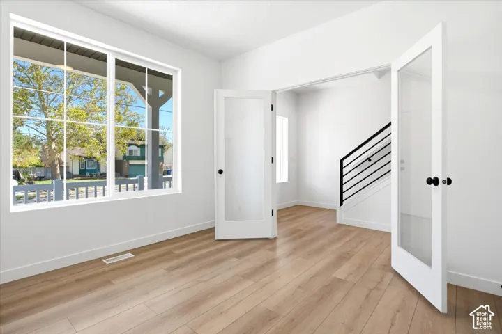 Light wood-finish flooring, white walls, large multi-pane window, double French doors with frosted glass, and black metal stair railing