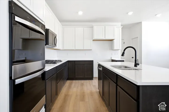 Kitchen featuring wood-finish flooring, two-tone cabinetry, white countertops, built-in stainless steel double ovens, and a black gooseneck faucet