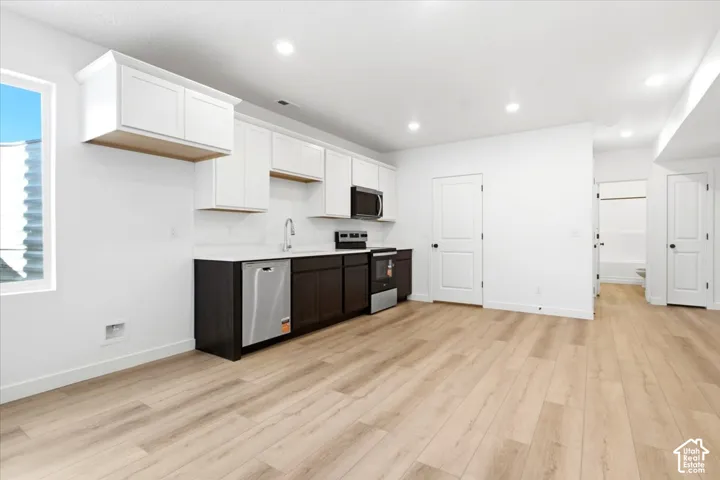 Open concept living area featuring wood-finish flooring, recessed lighting, and a modern kitchen with two-tone cabinetry and stainless-steel appliances