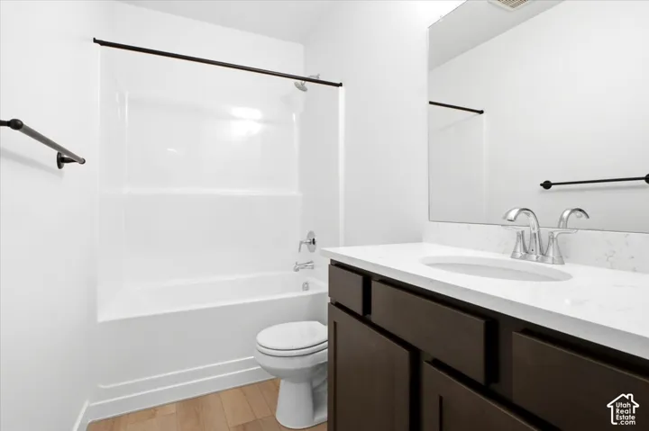 Tub and shower combination with chrome fixtures, wood-finish flooring, dark wood-finish vanity with an integrated sink, polished chrome faucet, and a wall-mounted mirror