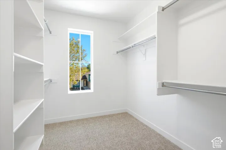 Custom white shelving, multiple hanging rods, window with white trim, light-toned carpet flooring