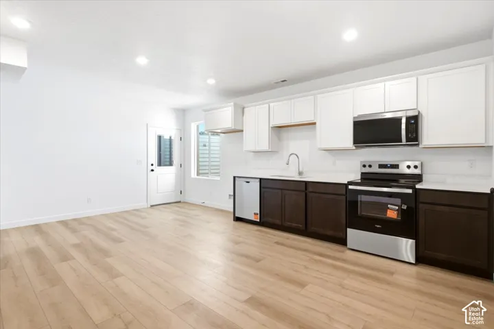Open-concept living space with wood-finish flooring, recessed lighting, and a kitchen featuring two-tone cabinetry, stainless steel appliances, and solid surface countertops