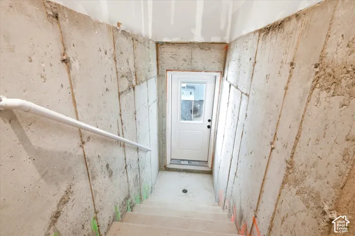 Stairwell with concrete walls, white handrail, and a white door with a window