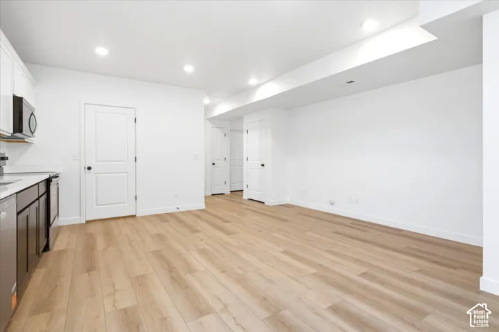 White cabinetry with stainless steel appliances, wood-finish flooring, recessed lighting, and a white countertop