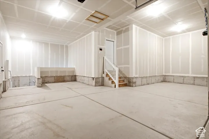 Concrete flooring, unfinished drywall, interior staircase with railing, recessed lighting, and exposed ceiling joists
