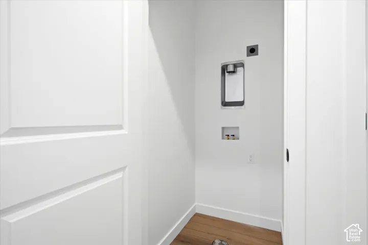 Laundry alcove with wood-finish flooring, white walls, and utility connections
