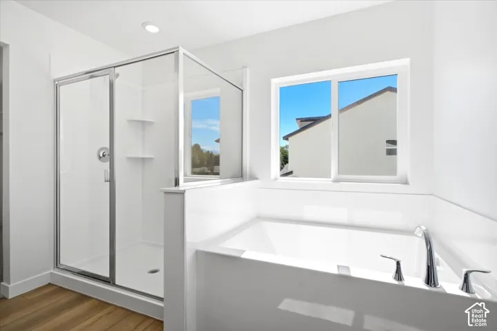 Built-in soaking tub with chrome fixtures, glass-enclosed shower, wood-finish flooring, and recessed lighting