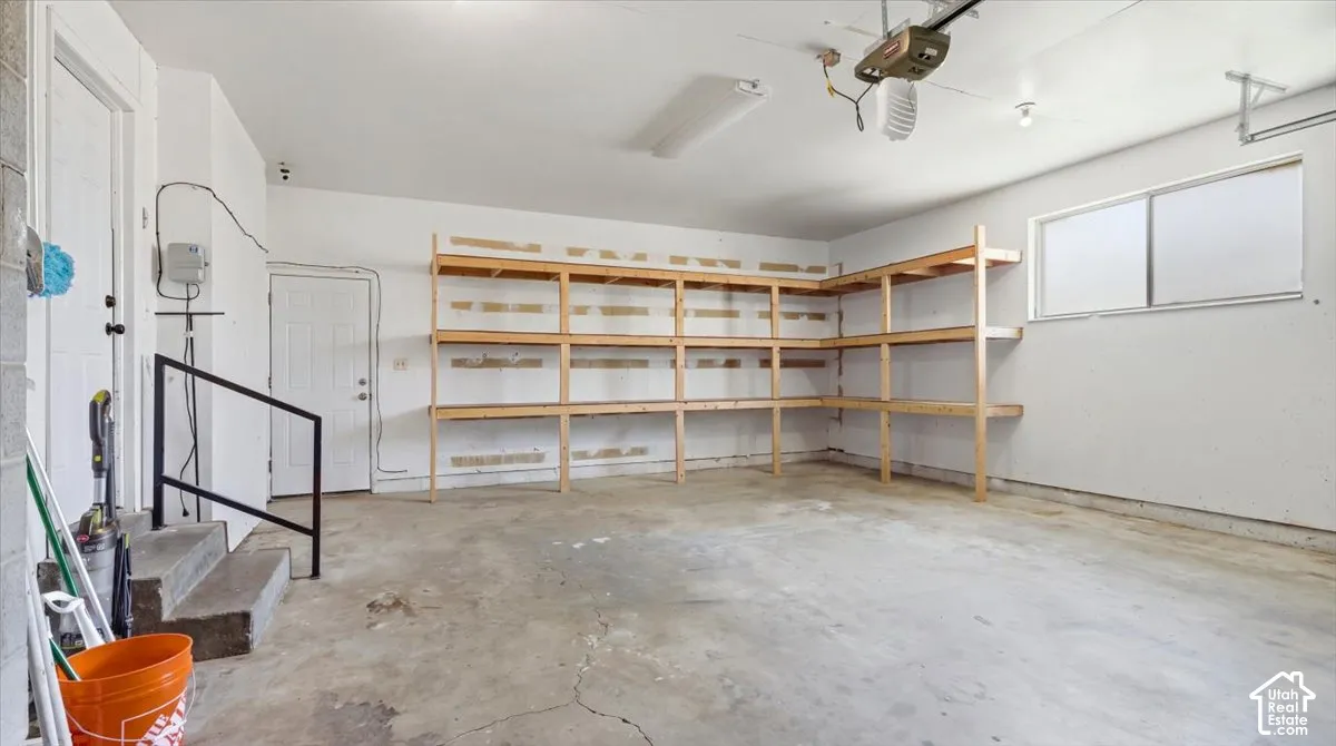 Attached garage with concrete flooring, built-in wooden shelving, and a window for natural light
