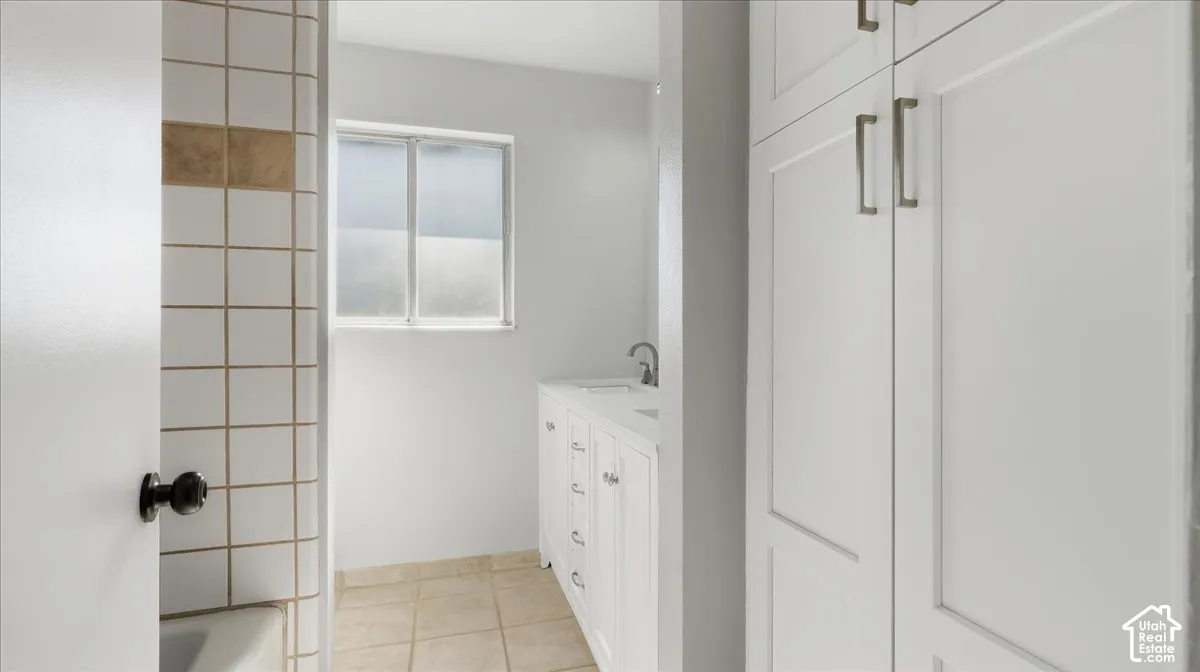 White panel cabinetry with brushed nickel hardware, white vanity with integrated sink, chrome faucet, and tiled shower surround
