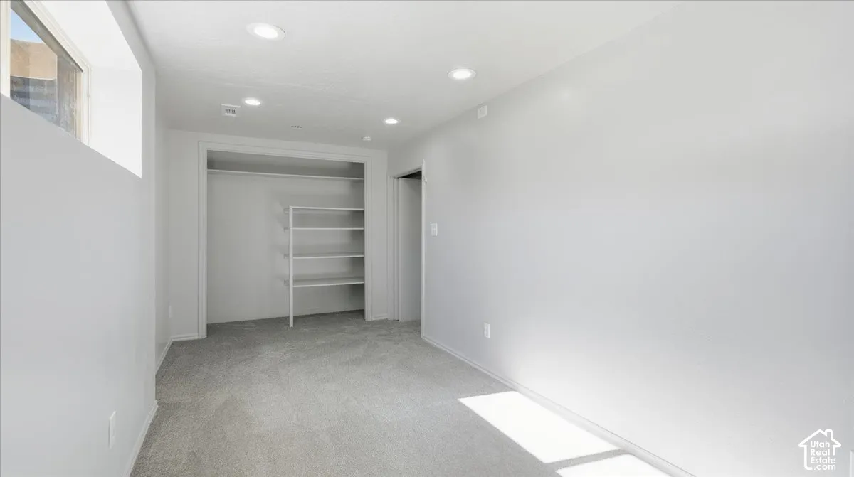 Recessed lighting, light gray carpeting, built-in closet shelving, and a high-set window