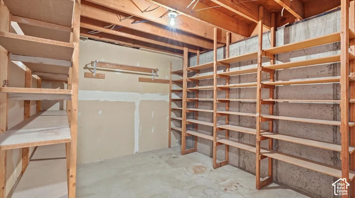 Extensive built-in shelving, exposed concrete foundation wall, wood beam ceiling, concrete flooring, and a wall-mounted hanging rack