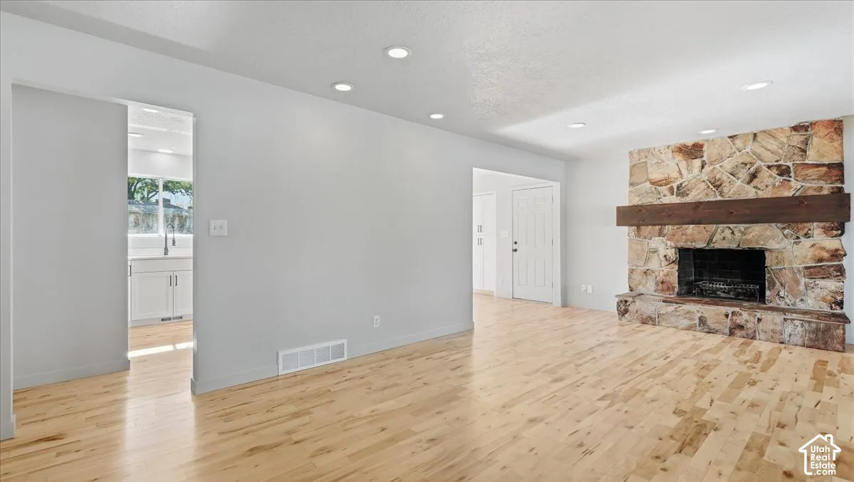 Expansive living area featuring light wood-finish flooring, recessed lighting, and a stone-clad fireplace with a substantial wood mantel