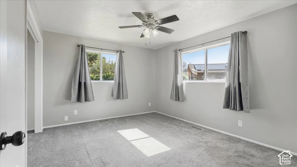 Neutral gray wall paint, gray carpeting, dual windows with curtains, and a ceiling fan with integrated lighting