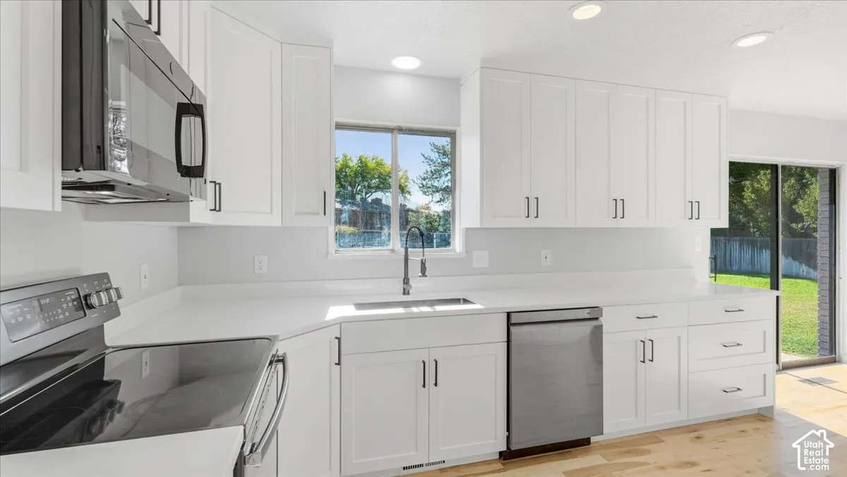 White shaker cabinetry, stainless steel appliances, light-toned countertops, and wood-finish flooring
