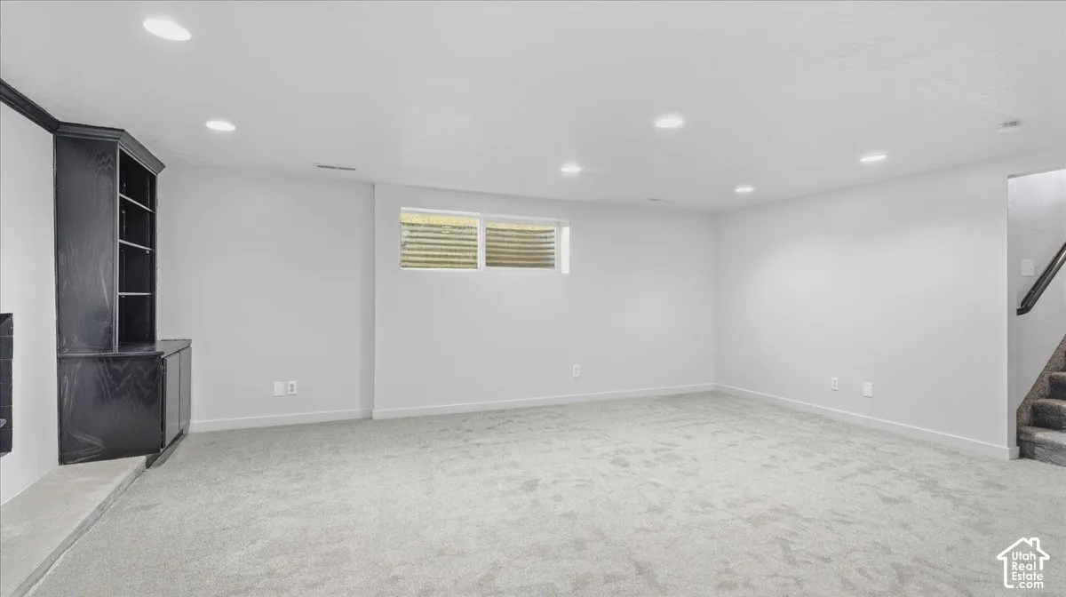 Recessed lighting illuminates a spacious room featuring light-toned carpeting and a built-in dark wood-finish shelving unit