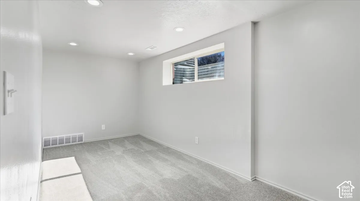 Recessed lighting, light gray carpeting, and white walls with a horizontal window