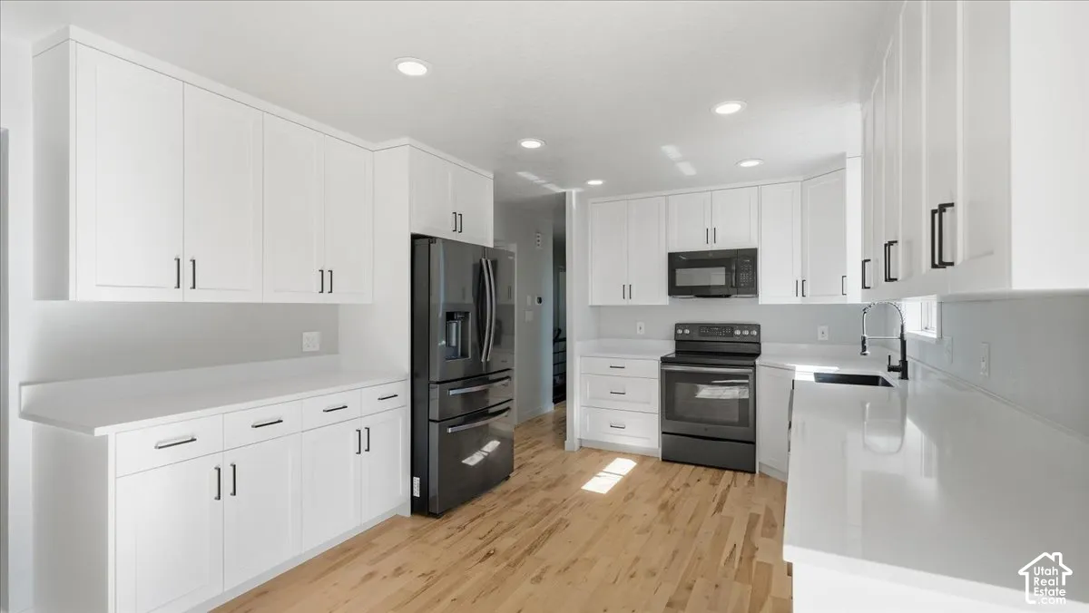 White cabinetry, dark appliance suite, light wood-finish flooring, recessed lighting, and solid surface countertops
