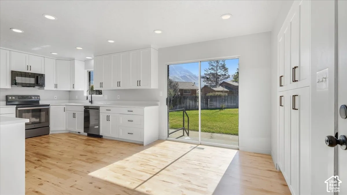 Kitchen featuring wood-finish flooring, white cabinetry, integrated range with microwave, and a sliding glass door to the backyard