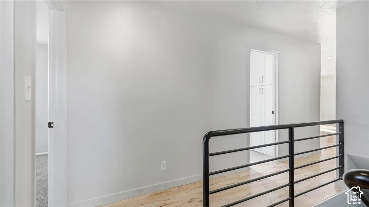 Light wood-finish flooring, white walls, black metal railing, and white built-in cabinetry