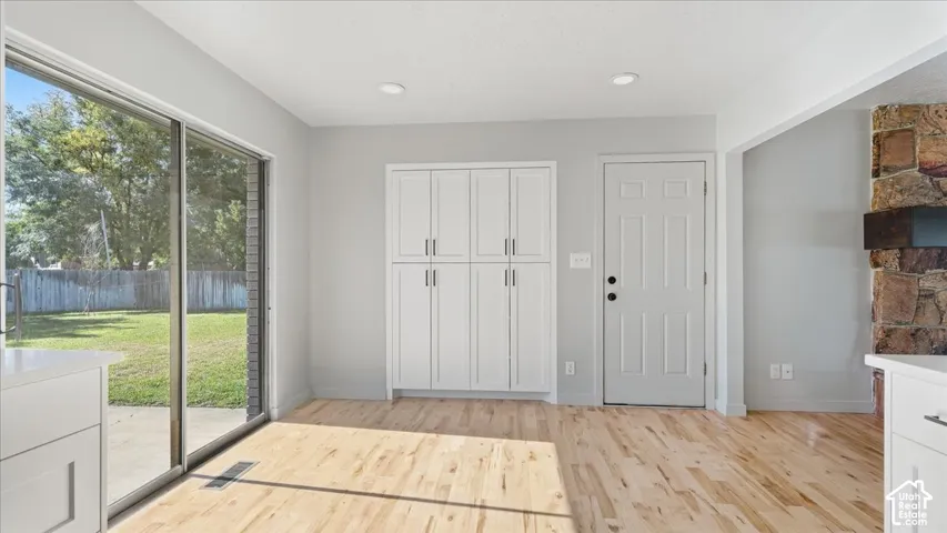 Sliding glass door, light wood-finish flooring, recessed lighting, white built-in cabinetry, and stone-clad fireplace
