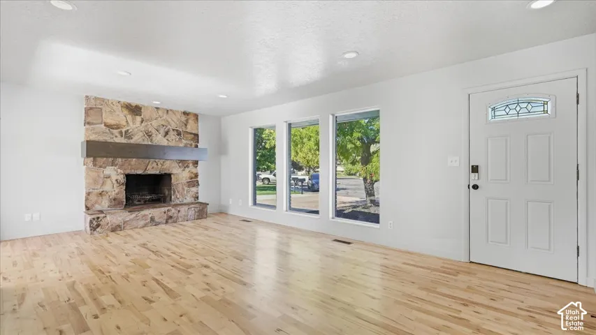 Spacious room featuring wood-finish flooring, a stone fireplace with a wood mantle, three panel windows, and recessed lighting
