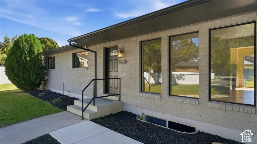 Gray brick exterior with dark trim and multiple large windows, featuring a front entry with a black door and exterior lighting