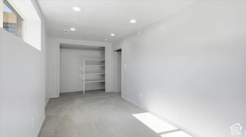 Recessed lighting, light gray carpeting, built-in closet shelving, and a high-set window