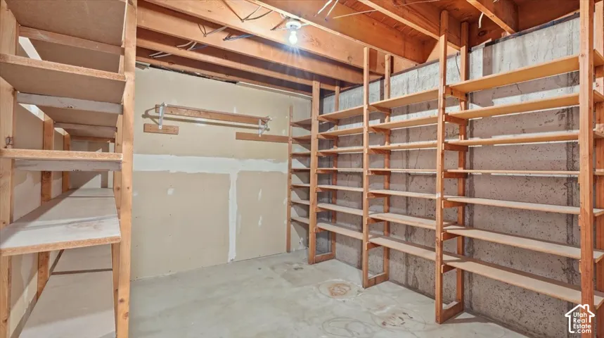 Extensive built-in shelving, exposed concrete foundation wall, wood beam ceiling, concrete flooring, and a wall-mounted hanging rack