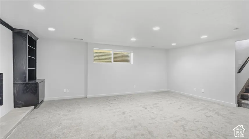 Recessed lighting illuminates a spacious room featuring light-toned carpeting and a built-in dark wood-finish shelving unit