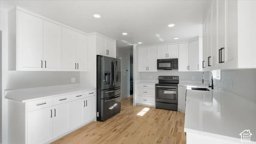 White cabinetry, dark appliance suite, light wood-finish flooring, recessed lighting, and solid surface countertops
