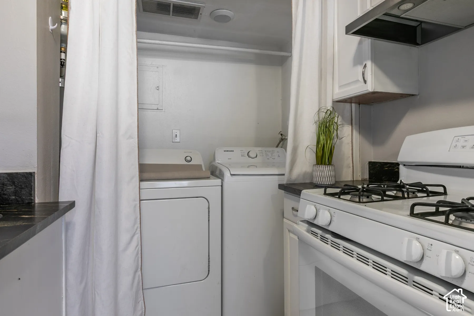 Built-in laundry appliances, white gas range, dark countertops, white upper cabinetry, and a stainless steel range hood
