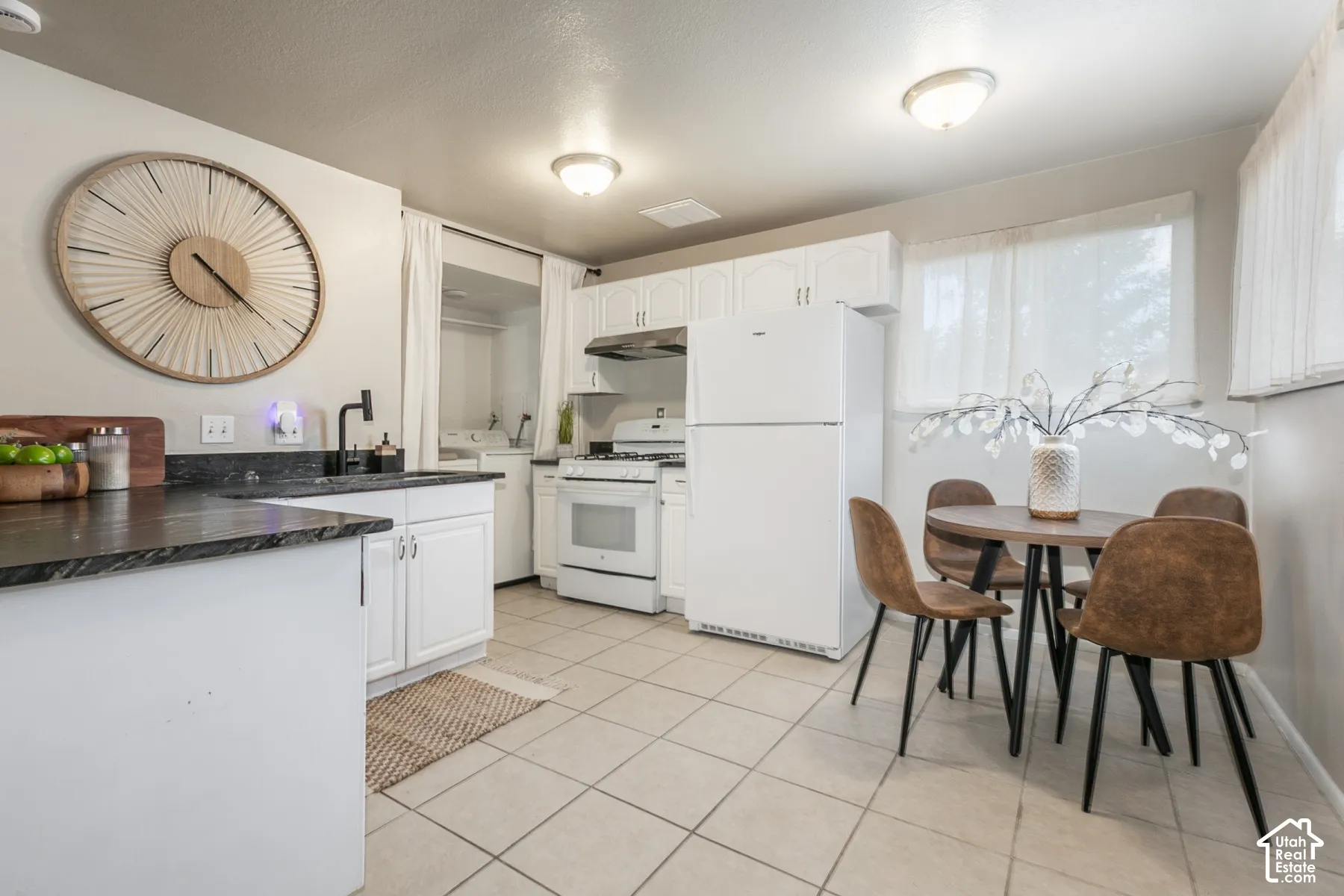 Kitchen featuring white cabinetry, dark countertops, a built-in sink with a matte black faucet, and white appliances