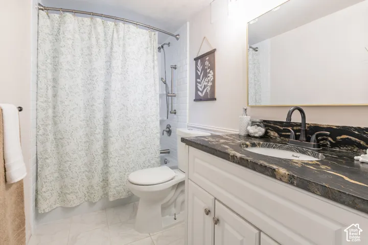 Bathroom featuring a white vanity with paneling, a dark countertop with gold veining, a wall-mounted mirror, a tiled shower with a handheld showerhead, and white floor tiles