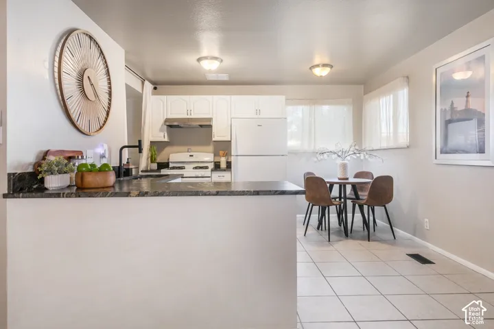 Kitchen featuring a dark stone-finish countertop, white cabinetry, and white appliances