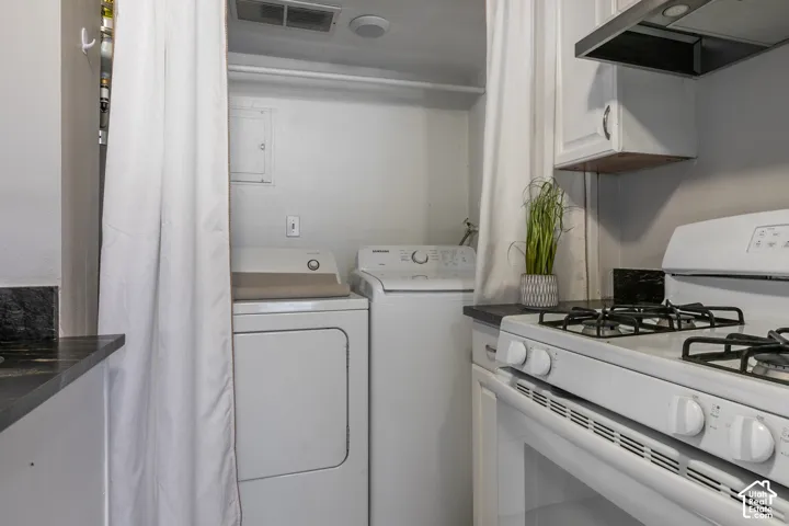 Built-in laundry appliances, white gas range, dark countertops, white upper cabinetry, and a stainless steel range hood