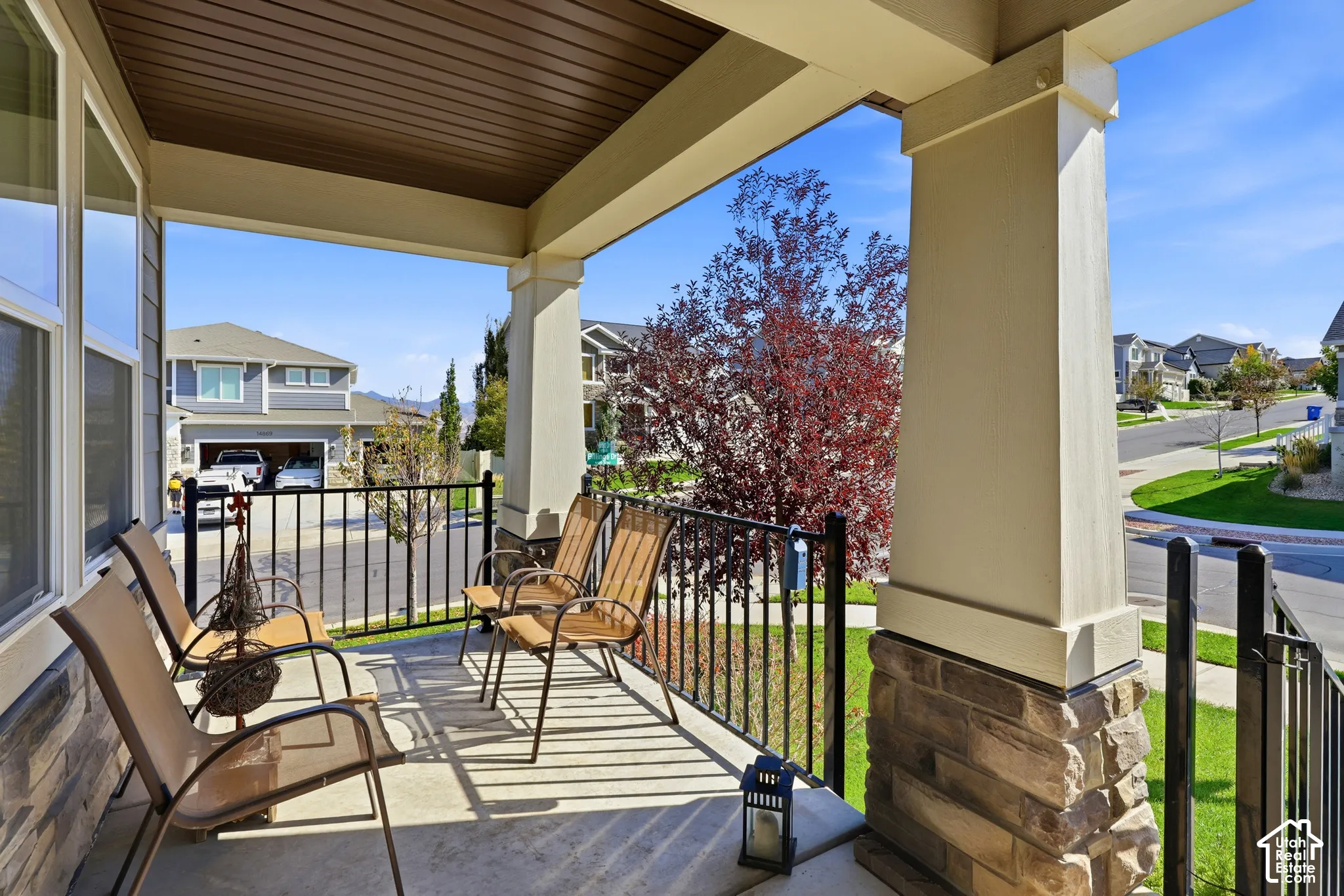 Covered front porch featuring a concrete surface, stone base columns, and black metal railings