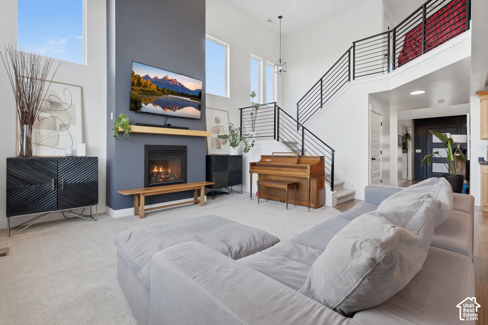 Two-story ceilings with high windows, an integrated fireplace, a wooden mantel, and a modern stair railing