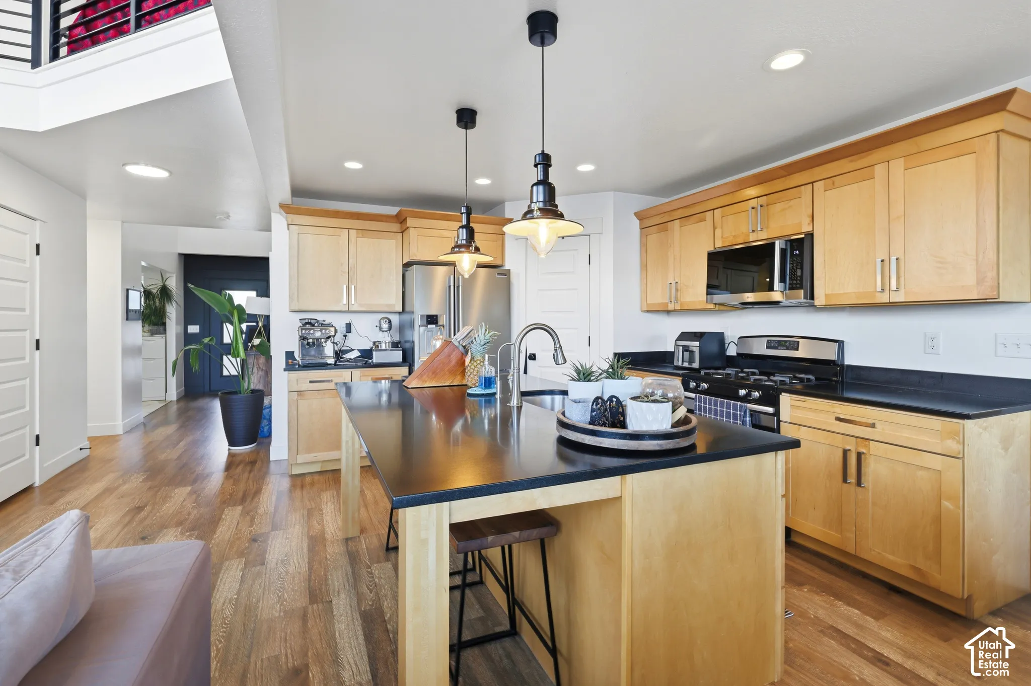 Kitchen featuring wood-finish flooring, light wood cabinetry, a center island with a dark countertop, stainless steel appliances, and pendant lighting